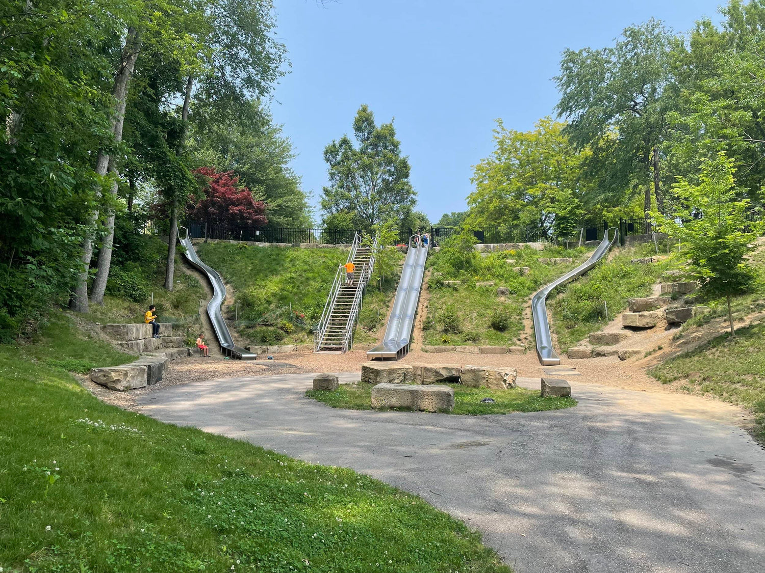 The Griff Slides consist of four metal slides. The area also features climbing stones, stone benches, and a decorative stone arch.